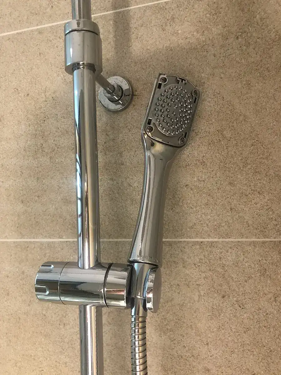 Chrome handheld shower head mounted on a slide bar against beige tile
