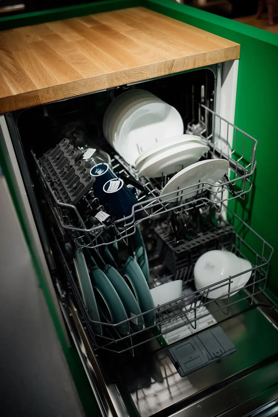 Loaded dishwasher with plates and bowls in its racks under a wood counter
