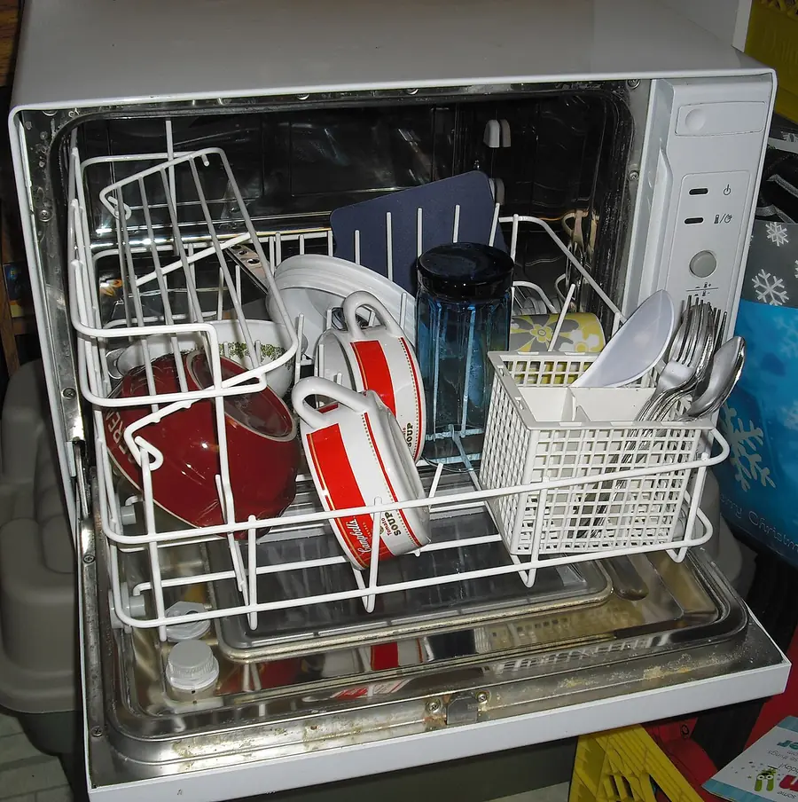 Open dishwasher with its racks pulled out holding dishes and utensils