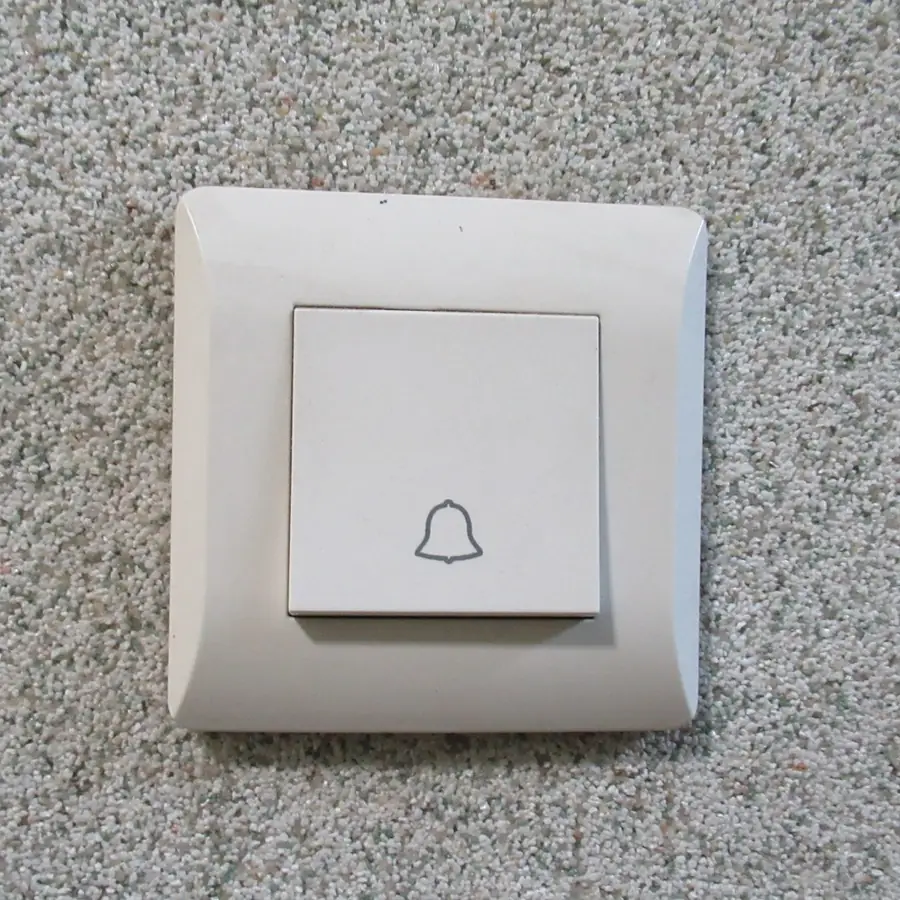 Square white doorbell button with a bell icon on a speckled wall