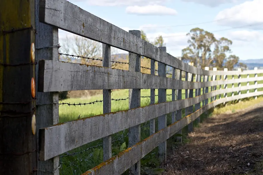 Weathered wood post and rail fence running along a grassy field