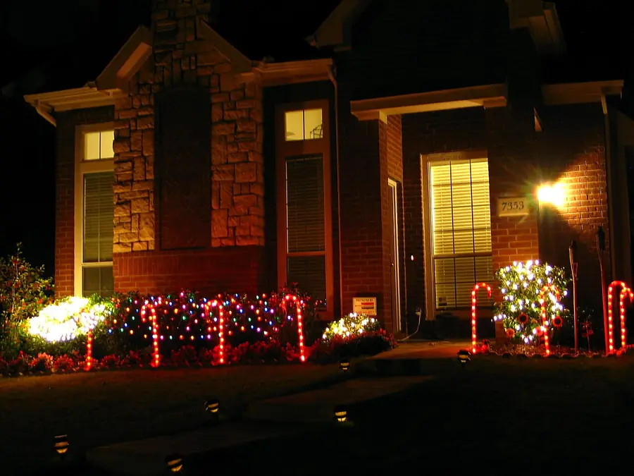 Brick house at night with colorful holiday lights along the shrubs and windows