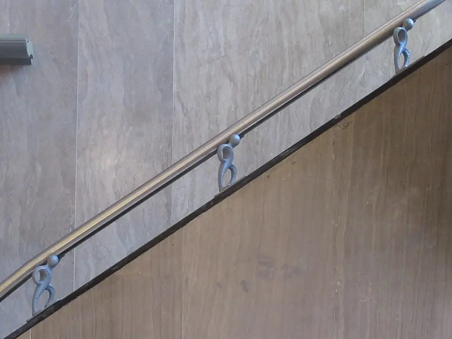 Long stainless steel handrail mounted with brackets along a stairway wall