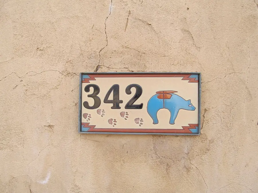 Painted ceramic address tile with a blue bear on a stucco wall