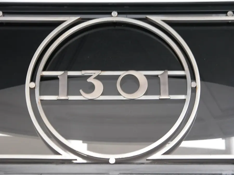 Metal house number sign inside a round decorative frame over a dark background
