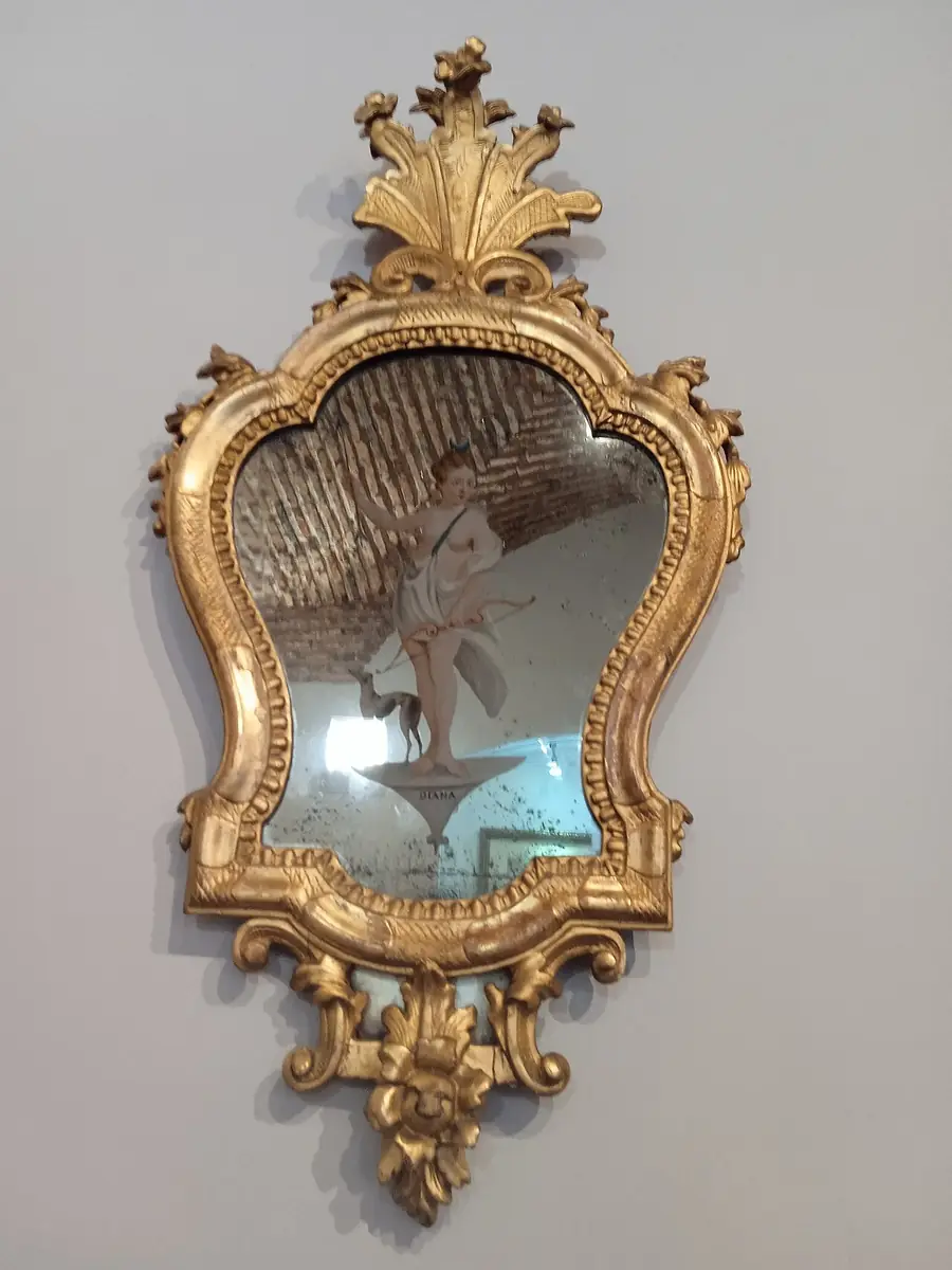 Small ornate gilded mirror with a carved crest hung on a white wall