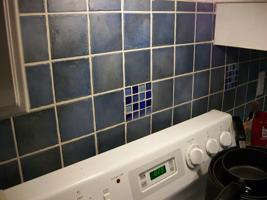 Blue ceramic tile backsplash with a glass mosaic strip above a stove