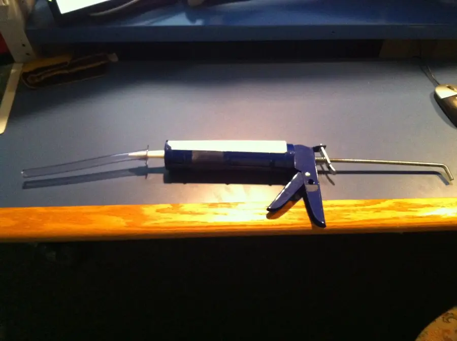 Blue caulk gun loaded with a tube resting on a wood ledge