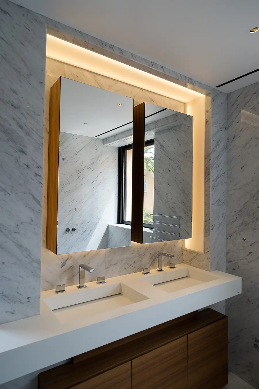Backlit LED mirror glowing above a double bathroom vanity with marble walls