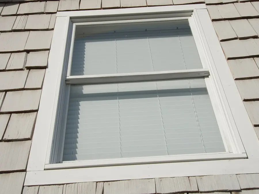 White double-hung window with blinds set in gray shingle siding