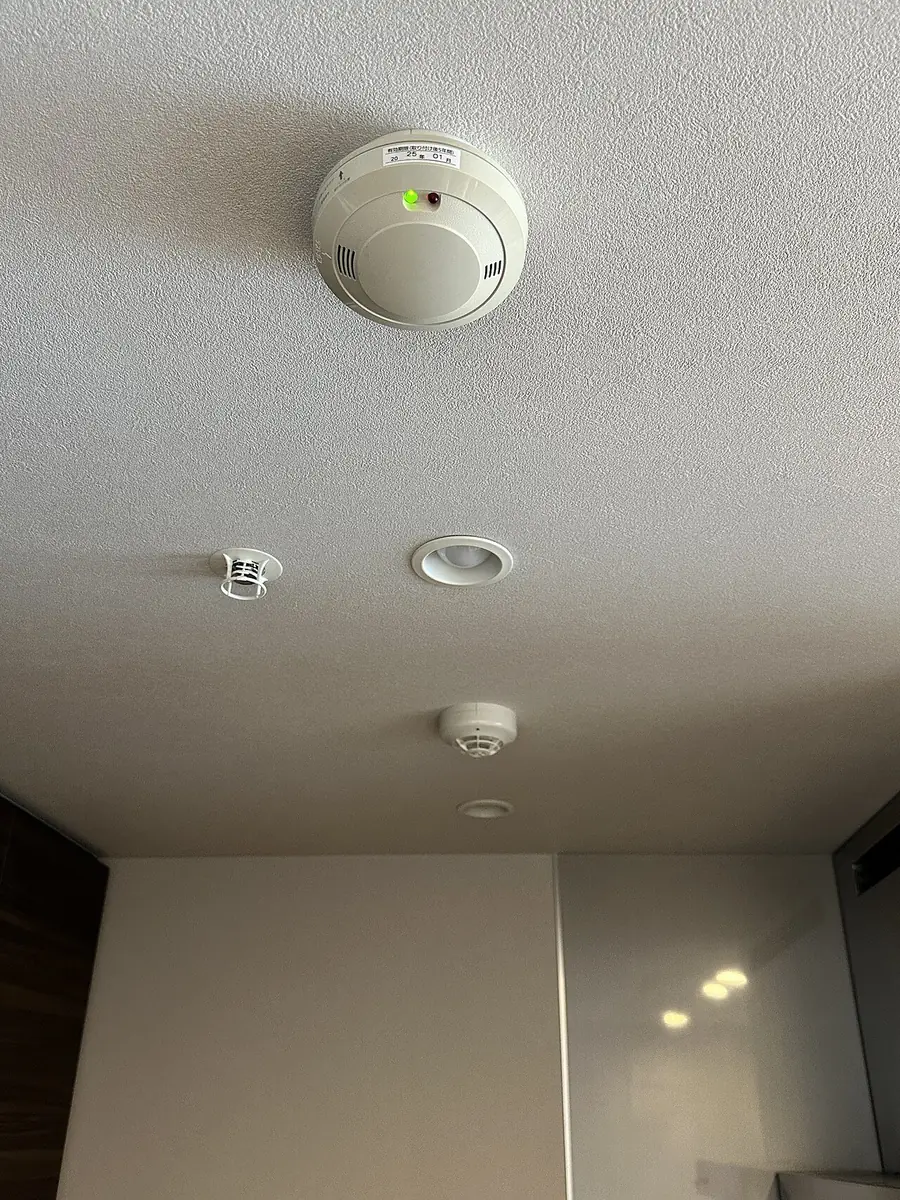 Round smoke detector mounted on a white ceiling near the wall