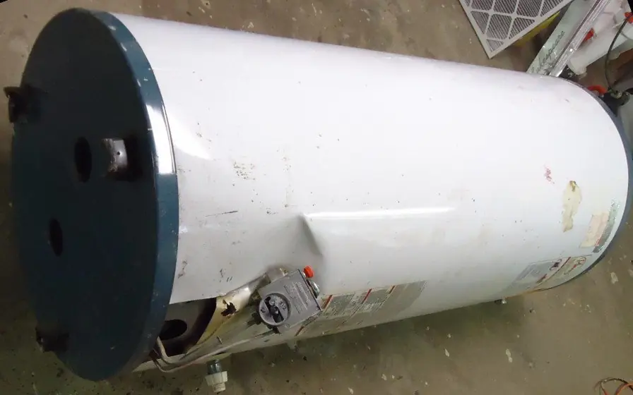 Old tank water heater removed and lying on its side on the floor