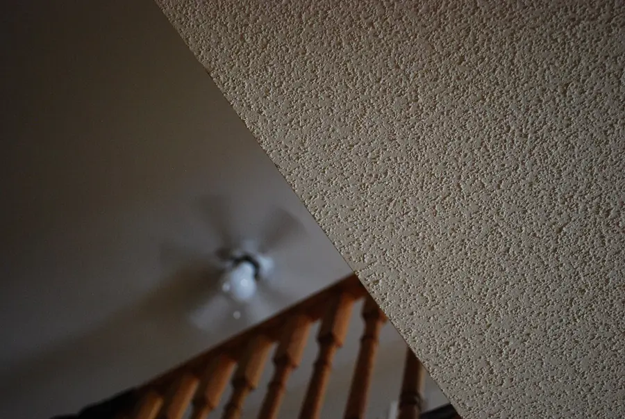 Popcorn textured ceiling above a staircase with a small ceiling light fixture