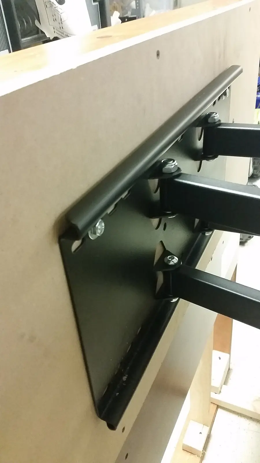 Black metal TV wall mount bracket bolted to a light colored wall