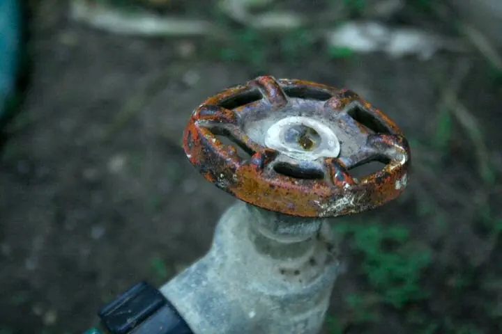 Rusty round handle on an old outdoor hose bib near the ground