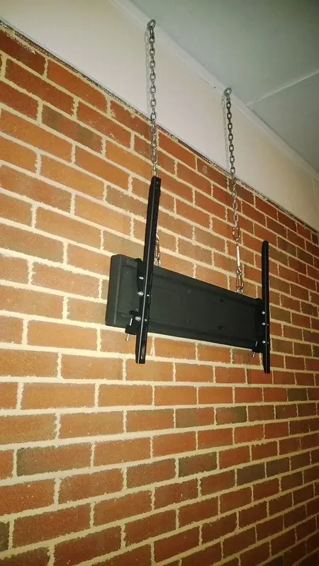 Flat TV wall bracket bolted to a red brick wall under a roof