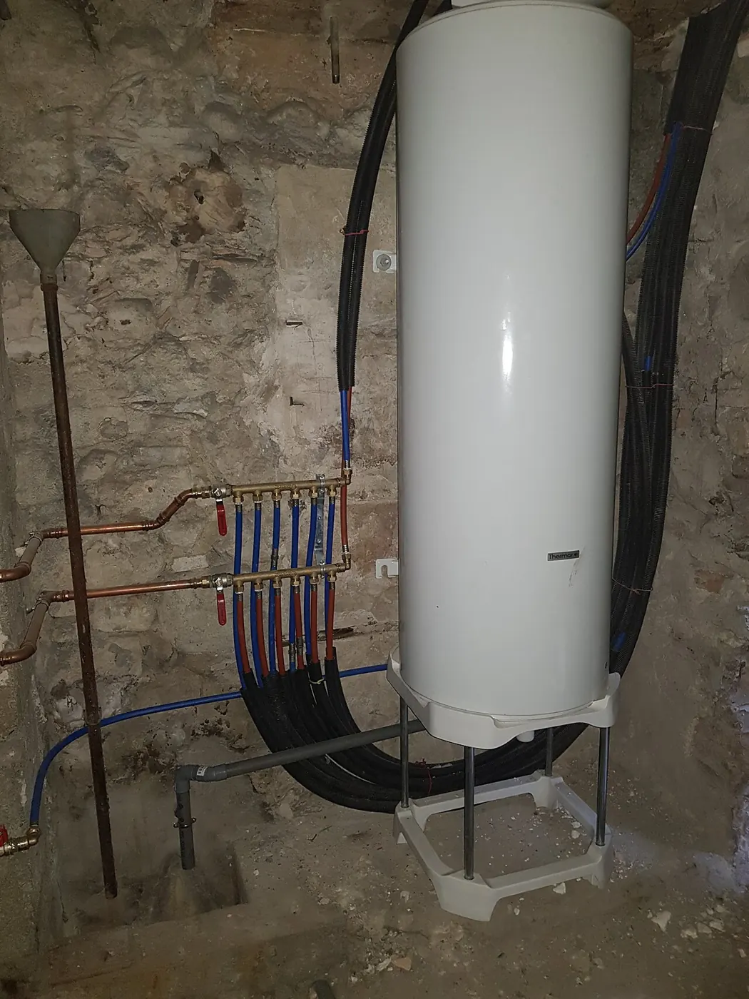 Wall-hung electric water heater beside a row of new supply pipes