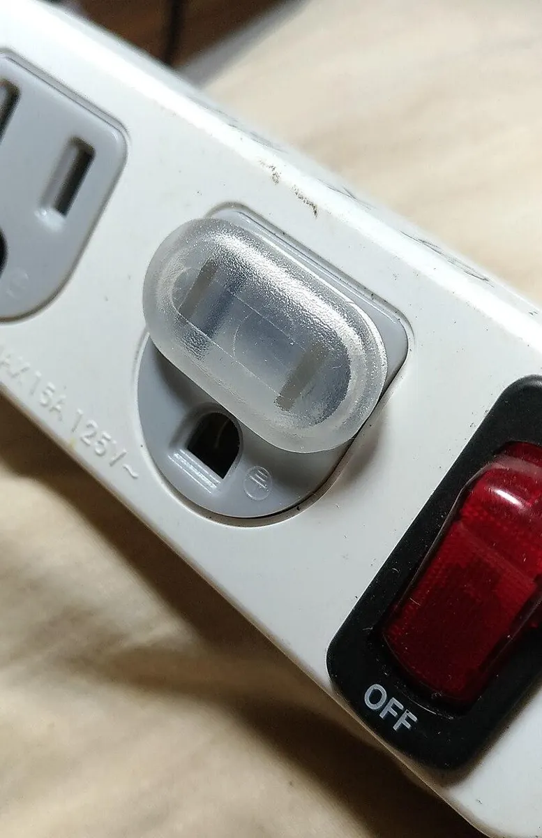 Clear plastic child safety cap plugged into one socket of a white power strip