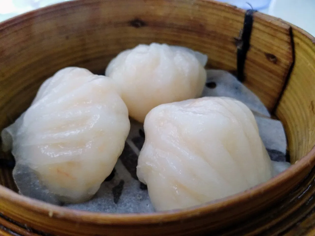 Three dim sum dumplings in a bamboo steamer basket