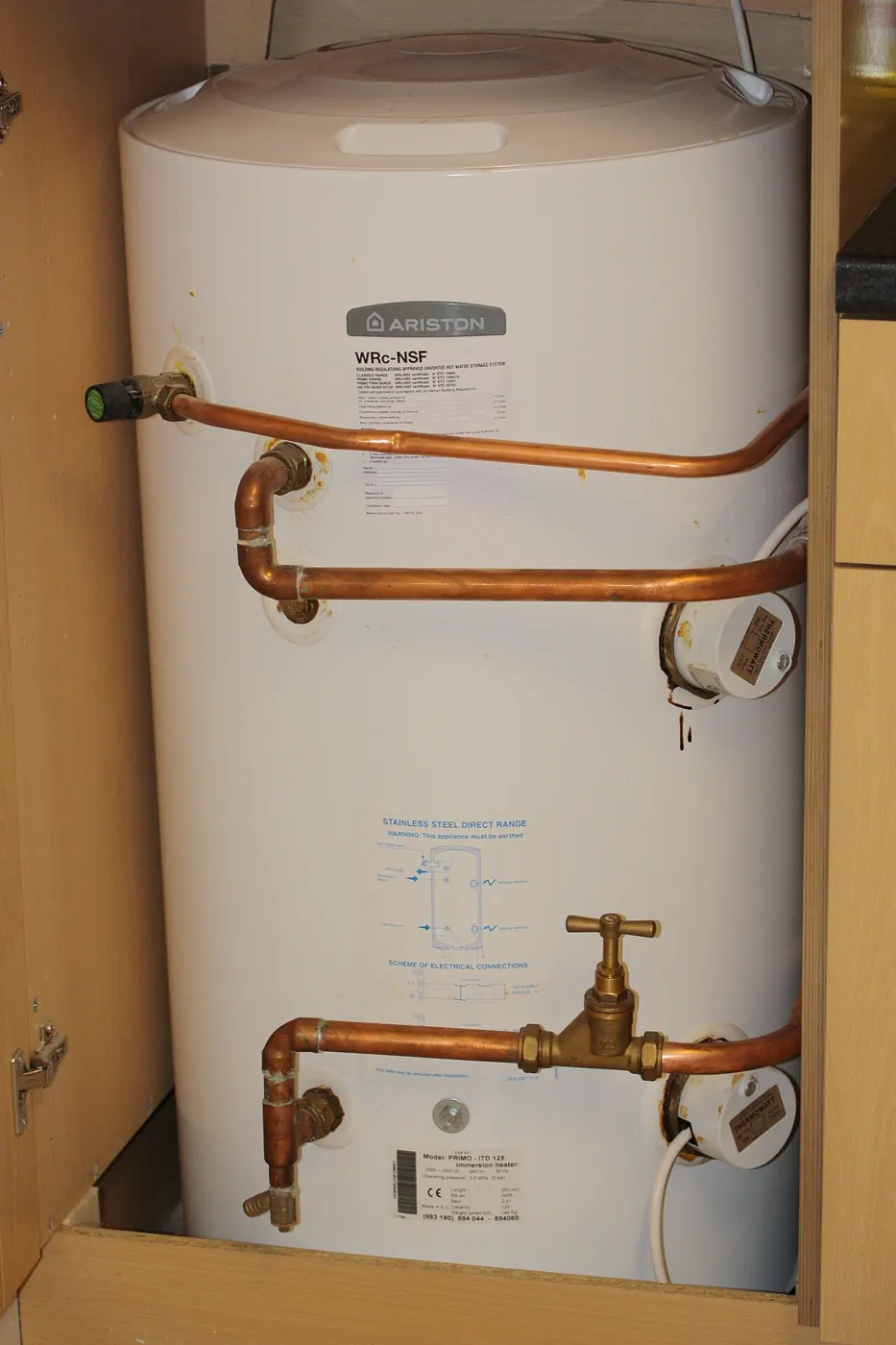 Electric hot water storage tank with its pipes in a cupboard