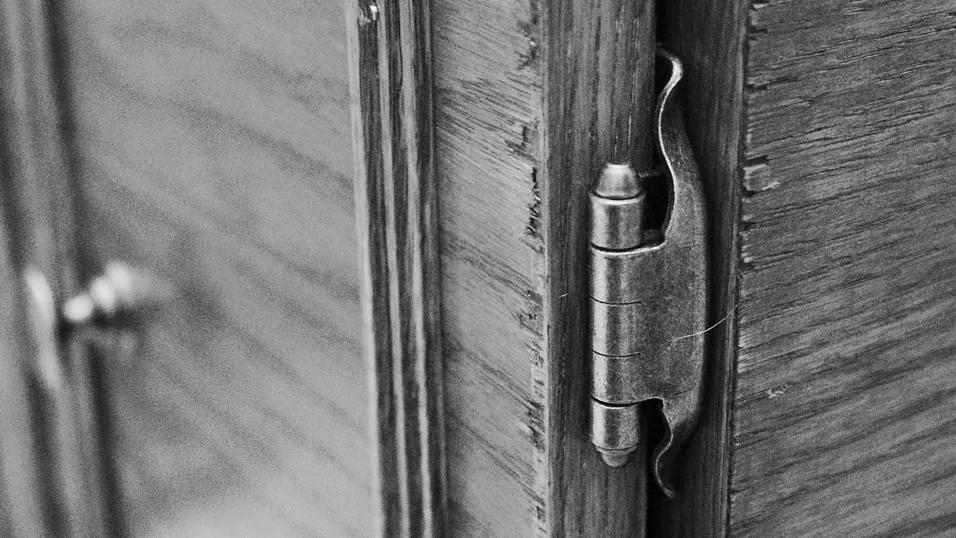 Black and white close-up of a door hinge on a wooden door