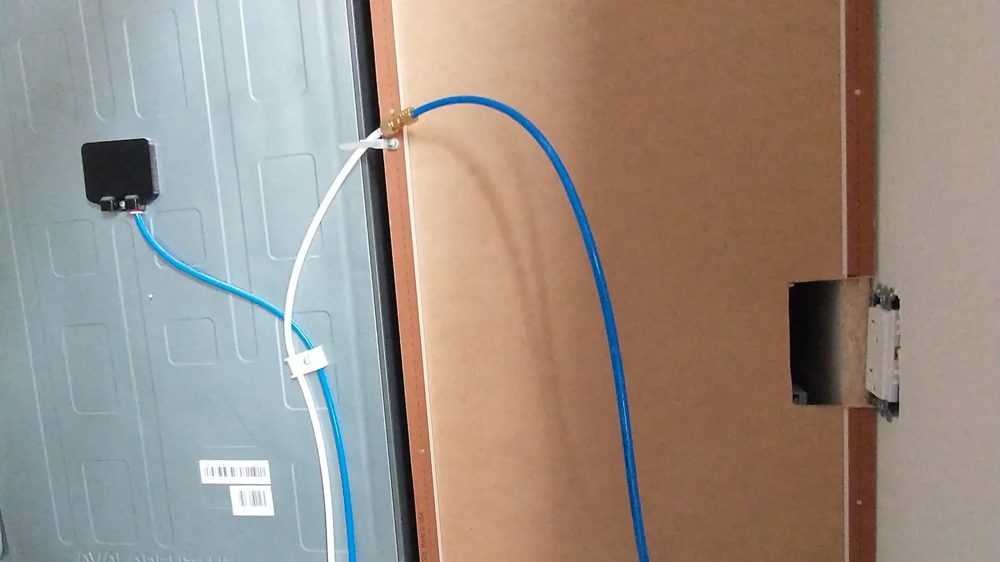Blue ice maker water line connected with a brass fitting to the back of a refrigerator