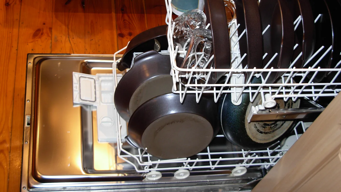 Built-in dishwasher with its door open and racks of pots and plates, between wood cabinets