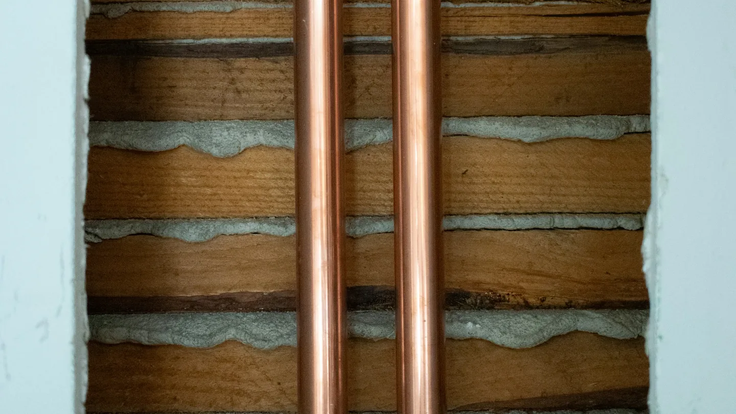 Two copper water pipes running through an opened plaster and lath wall