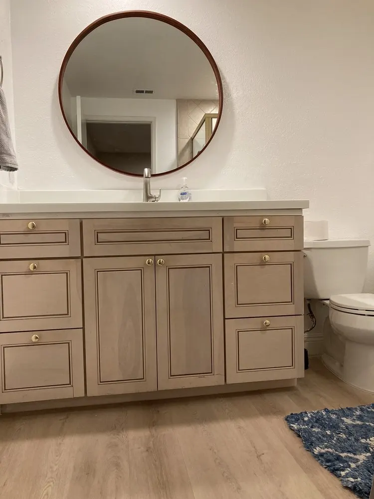 Light wood bathroom vanity with shaker cabinet doors and drawers under a round mirror