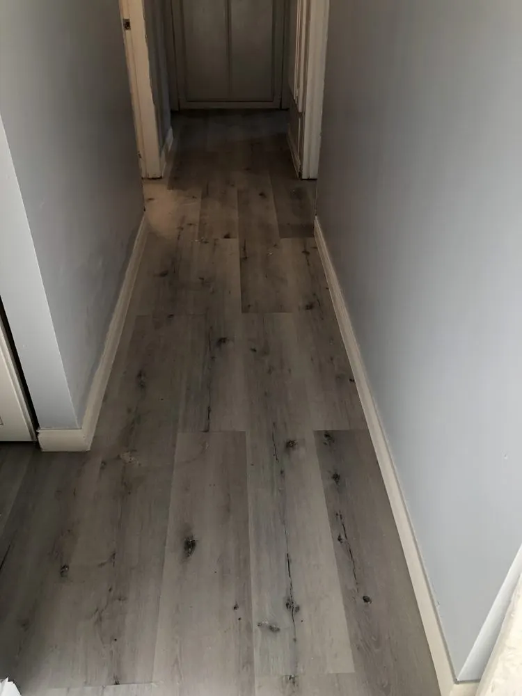 Long hallway with white baseboards running along new plank flooring