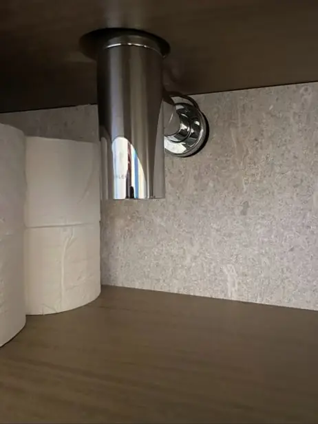 Chrome drain tailpiece and connection under a sink against a speckled wall