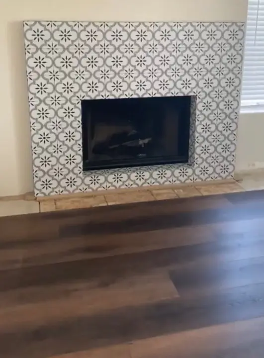 Fireplace surround finished in patterned cement tile above a dark wood floor