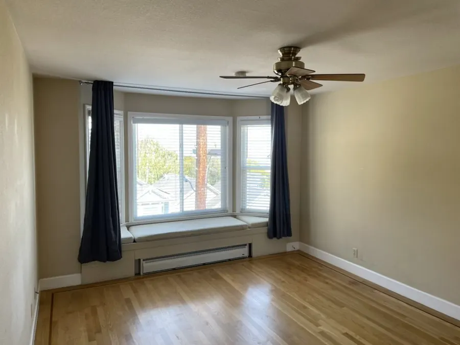 Bedroom window with dark curtains hung on a rod below a ceiling fan