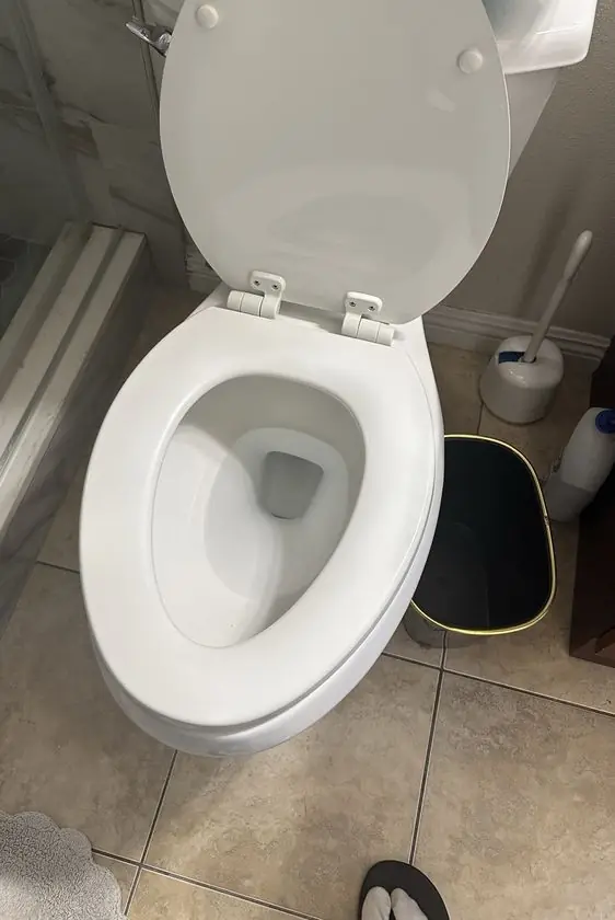 White elongated toilet with the seat up on a tile bathroom floor