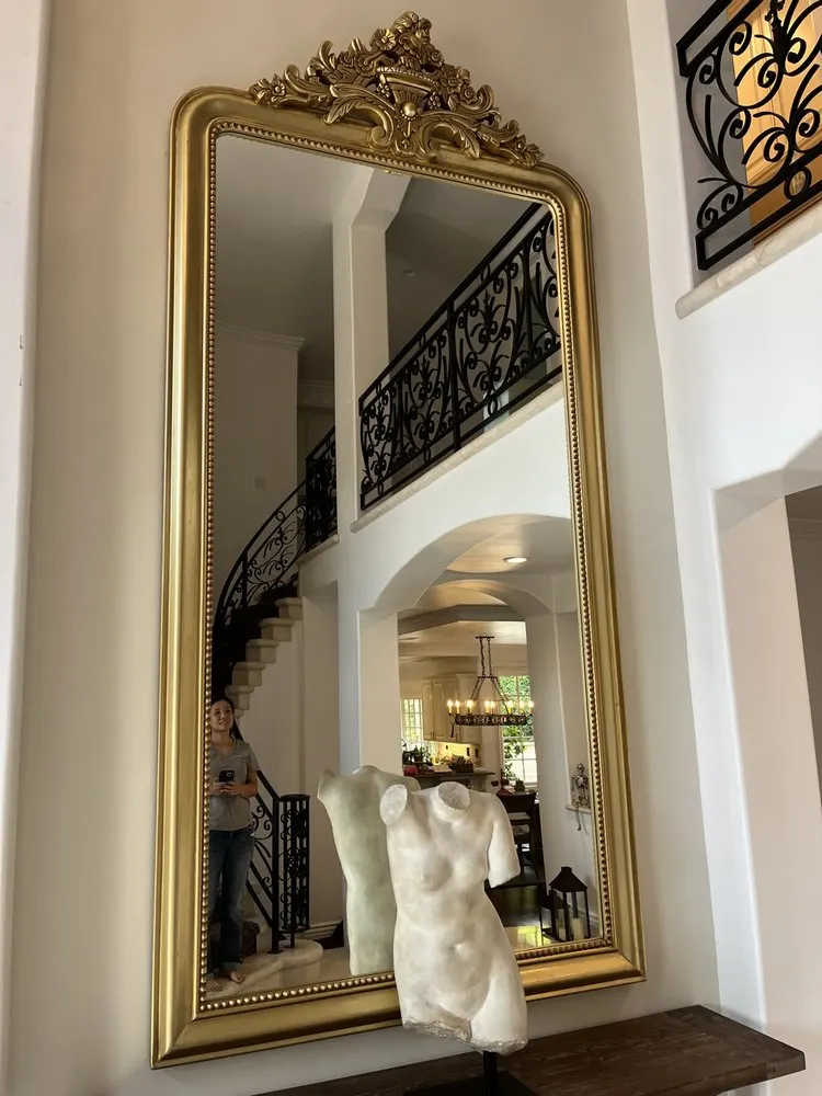Tall gold-framed mirror hung in a two-story entry